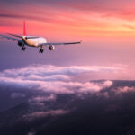 Airplane. Landscape with big white passenger airplane is flying in the red sky over the clouds at colorful sunset. Journey. Passenger airliner is landing at dusk. Business trip. Commercial plane